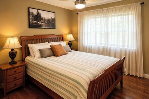 A bedroom with a wooden bed, two bedside tables with lamps, a large window with sheer curtains, and a framed picture on the wall. - Unwind Near the Lake Fire Pit Marina Nearby (Bronston)