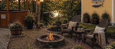 A cozy outdoor seating area with a fire pit, wooden chairs, and potted plants.