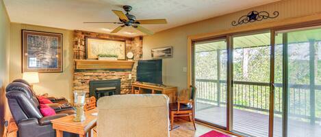 A living room with a stone fireplace, leather recliner, flat-screen TV, and a large sliding glass door to the outdoors.