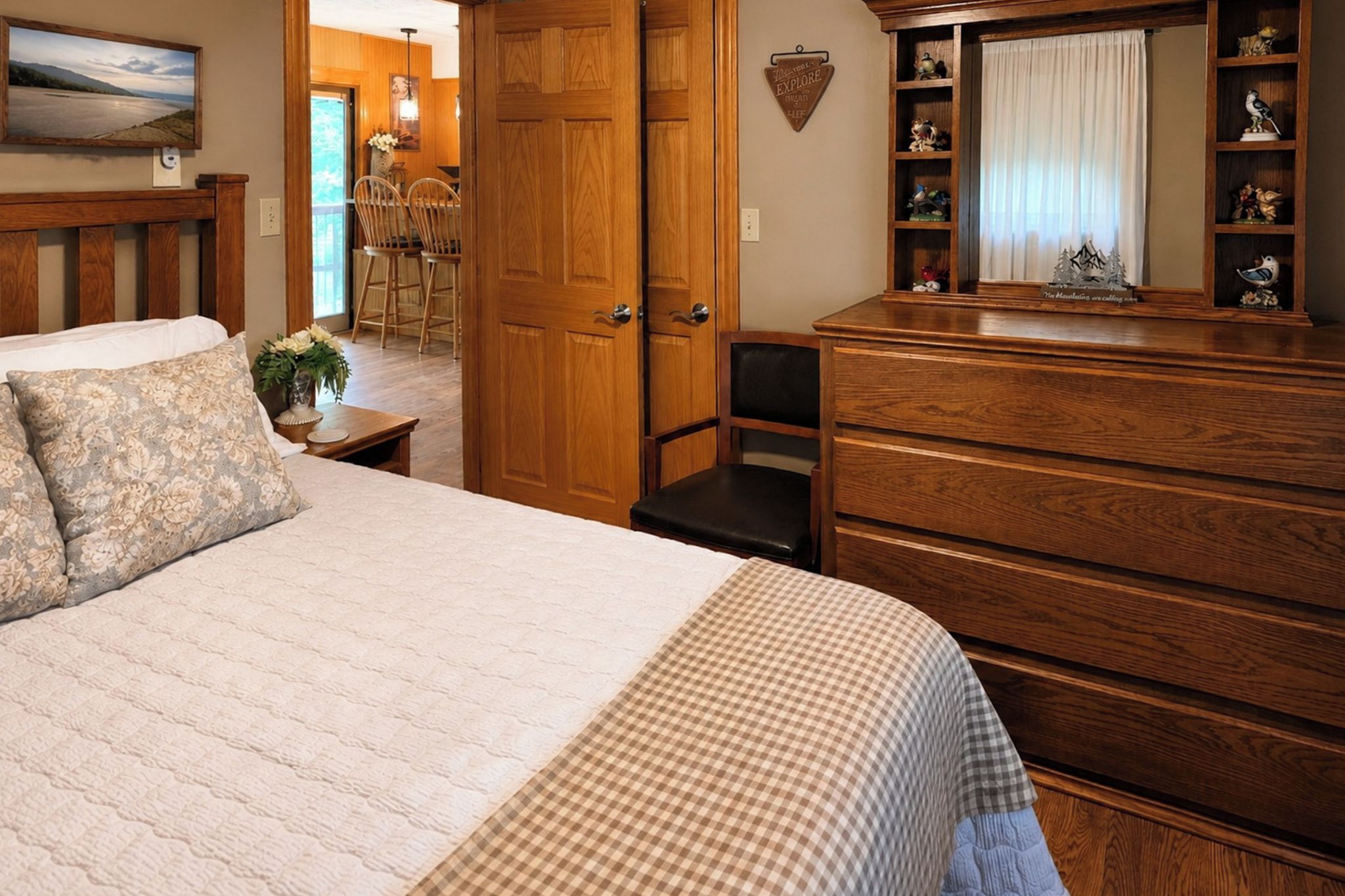 Un dormitorio con cama, cómoda y puerta de madera que da a un comedor.
