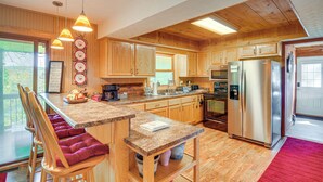 A kitchen with wooden cabinets, a stainless steel refrigerator, and a breakfast bar with chairs. - Unwind Near the Lake Fire Pit Marina Nearby (Bronston)