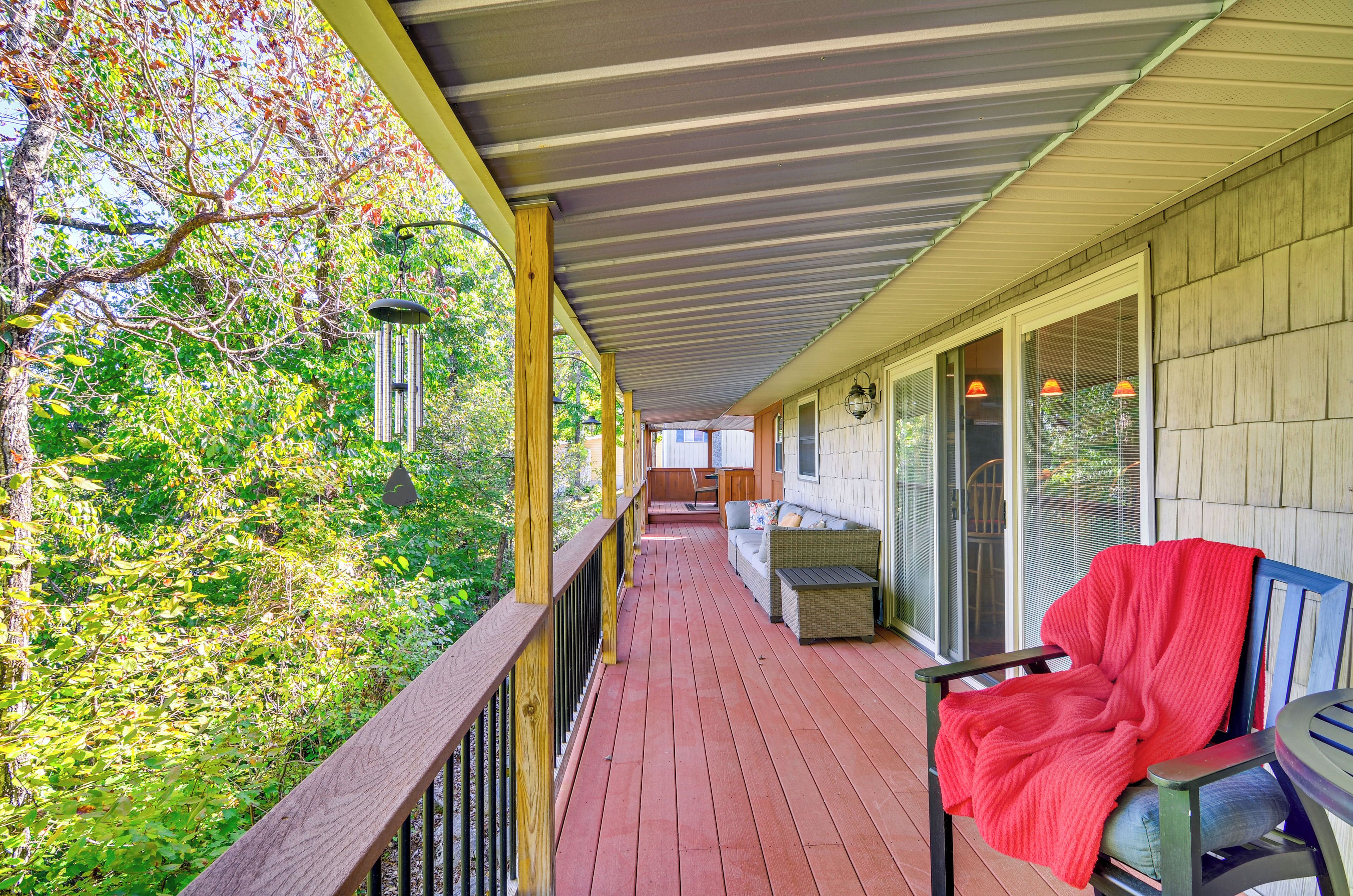 A covered porch with a wooden deck, a sofa, and a chair with a red blanket.