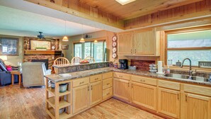 A kitchen with wooden cabinets, granite countertops, and a built-in stove. There is a dining area with a table and chairs, and a living room with a couch and a coffee table. - Unwind Near the Lake Fire Pit Marina Nearby (Bronston)