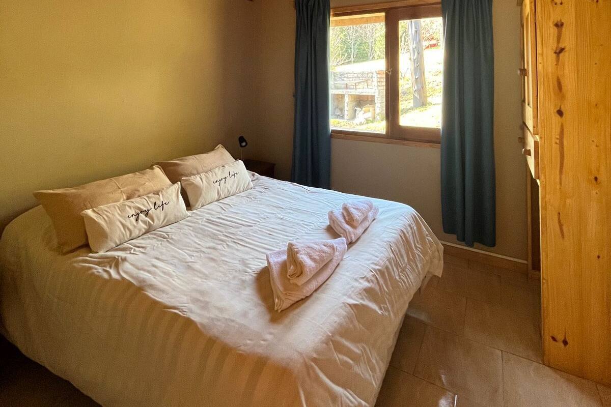 Una habitación con paneles de madera, una cama, una ventana con cortinas y un armario de madera.