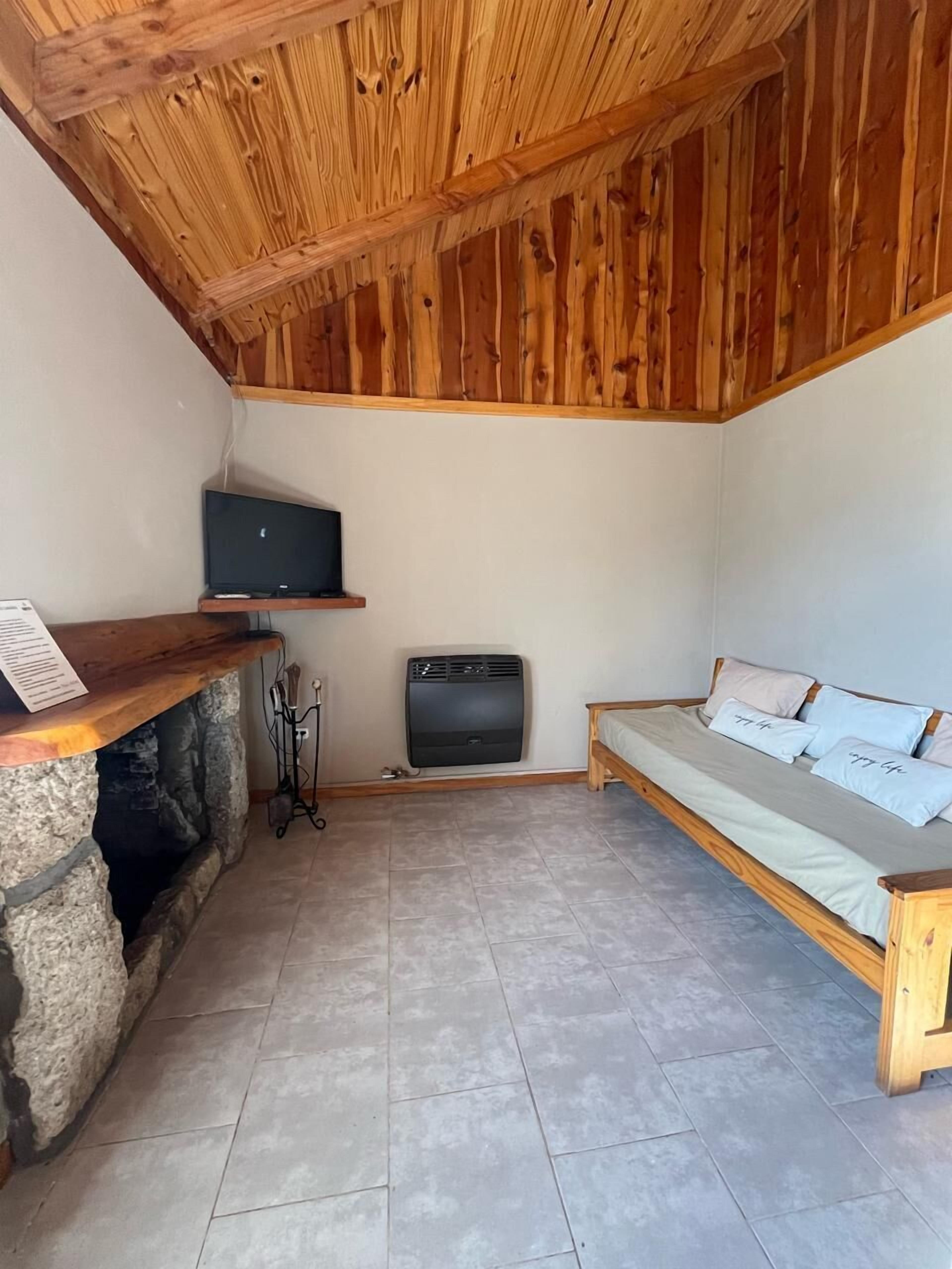 Une pièce avec une cheminée en pierre, un téléviseur fixé au mur, un canapé avec des coussins et un plancher carrelé.