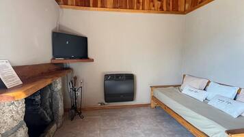 Une pièce avec une cheminée en pierre, un téléviseur fixé au mur, un canapé avec des coussins et un plancher carrelé.