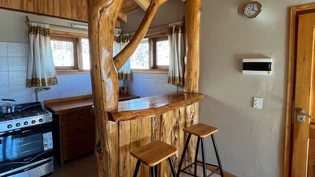 A kitchen with a wooden island, two stools, a stove, and a sink. - Cabañas Rayen  (Villa Traful)