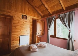 A wooden cabin room with a bed, a wardrobe, and a window with curtains.