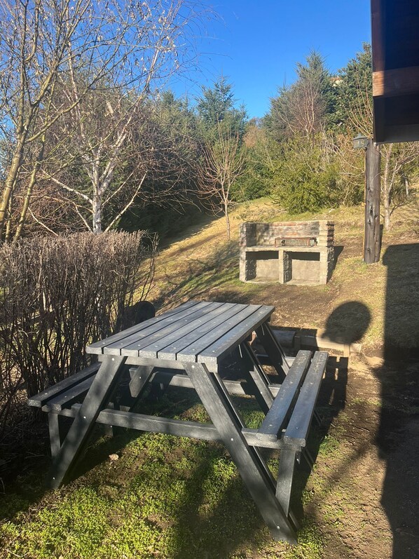 A picnic table set in a natural outdoor area with a stone bench in the background.