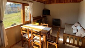 A cozy room with a wooden ceiling, a dining table with chairs, a sofa, a television, and a stone fireplace. - Cabañas Rayen  (Villa Traful)