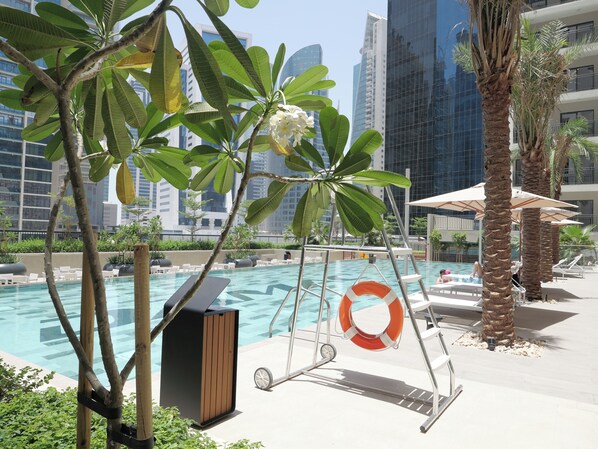 Relax by the serene pool surrounded by lounge chairs and umbrellas, amidst a lush garden and palm trees.