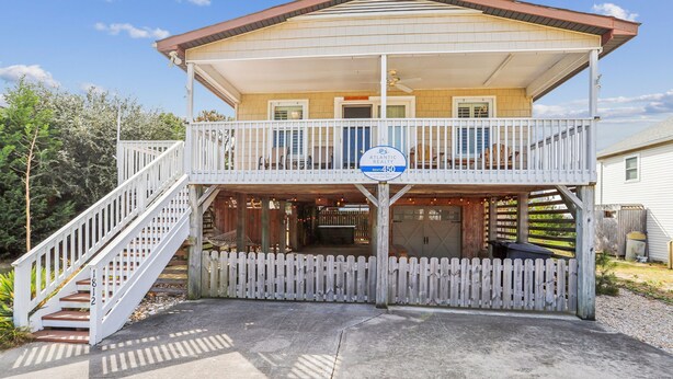 A two-story house with a balcony, a porch, and a sign indicating a rental price of $450. - Sea Glass Shack -- Pet Friendly with Hot Tub (Kill Devil Hills)