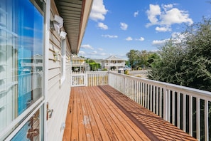 Um deck de madeira com guarda-corpo branco, com vista para uma área residencial com casas e árvores.
