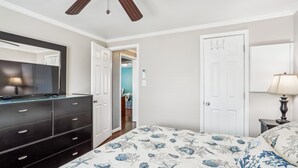 A bedroom with a bed, dresser, ceiling fan, and a door leading to another room. - Sea Glass Shack -- Pet Friendly with Hot Tub (Kill Devil Hills)