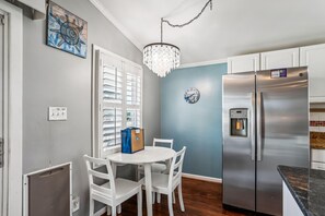 A kitchen with white cabinets, a stainless steel refrigerator, a water dispenser, and a dining table with chairs.
