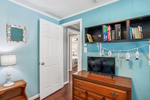 A room with teal walls, a white door, a wooden dresser, a television, and a bookshelf with books and games.