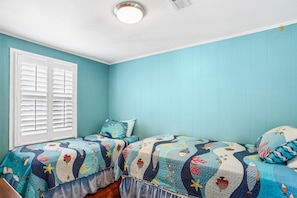 A bedroom with two beds, a window with shutters, and a ceiling light.