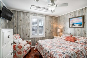Un dormitorio con cama, cómoda, silla, un cuadro y ventilador de techo.