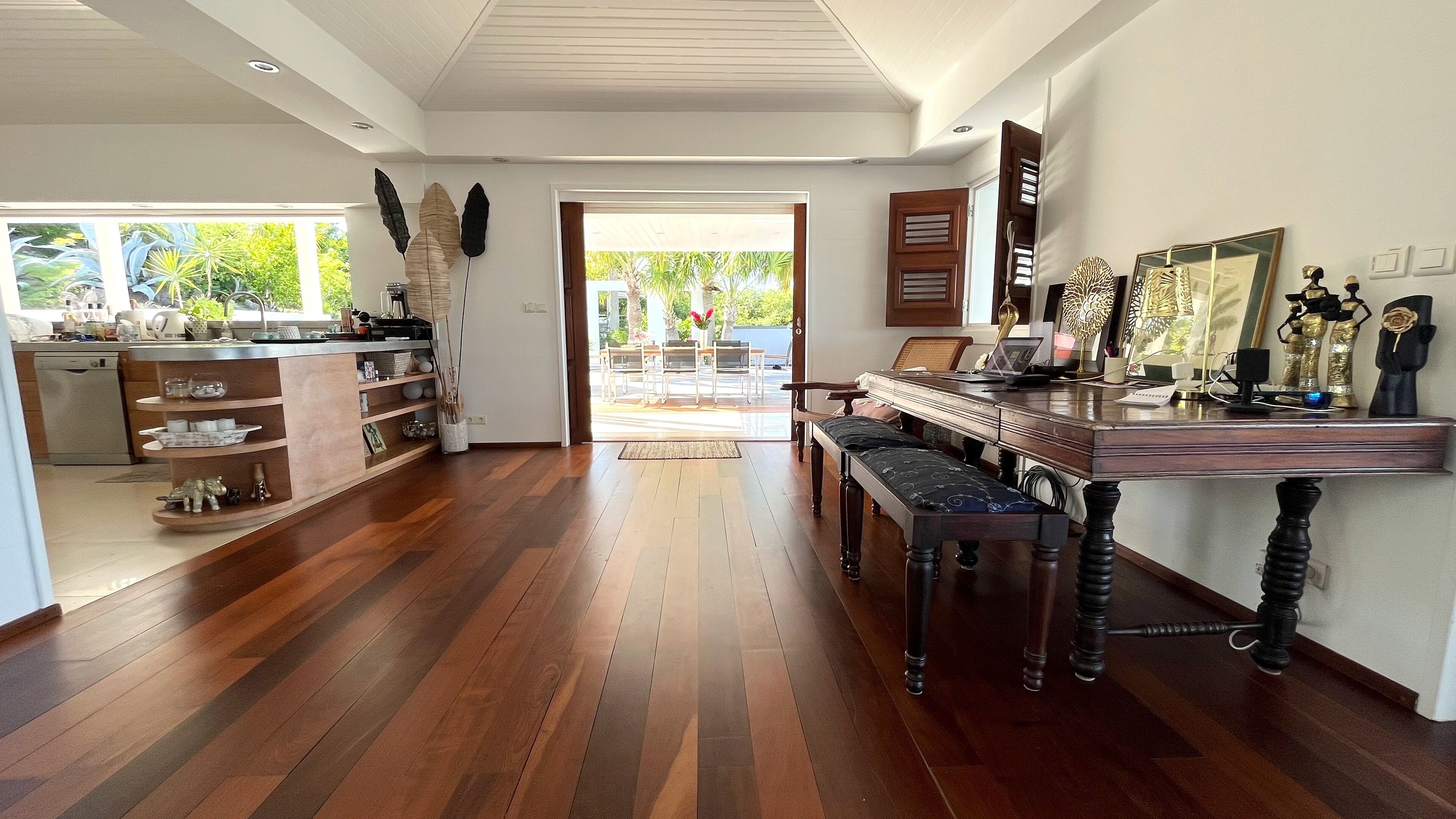 A spacious room with a wooden floor, a dining area with a piano, and a kitchen with a dishwasher.