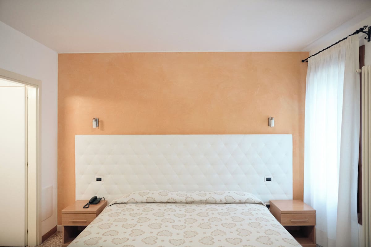 Ein Hotelzimmer mit einem großen Bett, zwei Nachttischen, einem Wandthermostat und einem Beistelltisch.