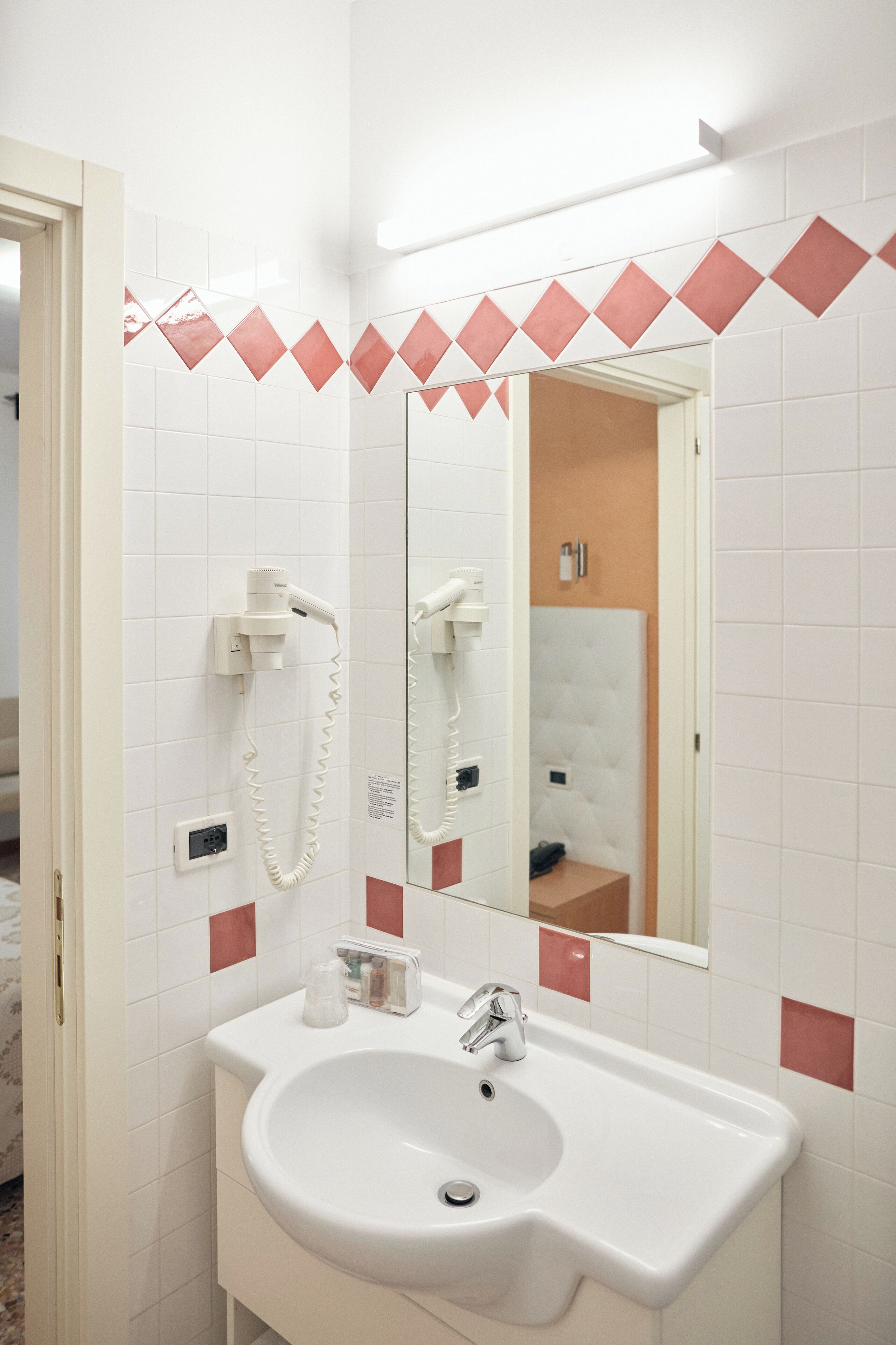 A bathroom with a white sink, a mirror, and a hairdryer mounted on the wall.