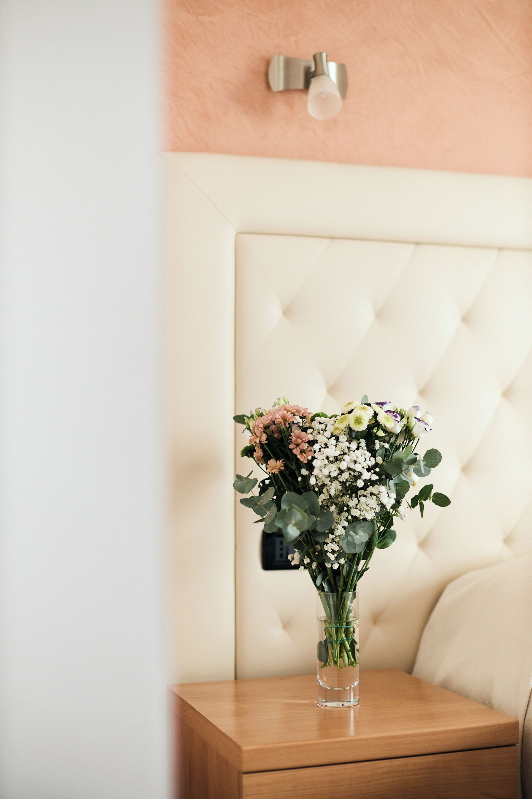 A bedside table with a clear glass vase containing a bouquet of flowers.