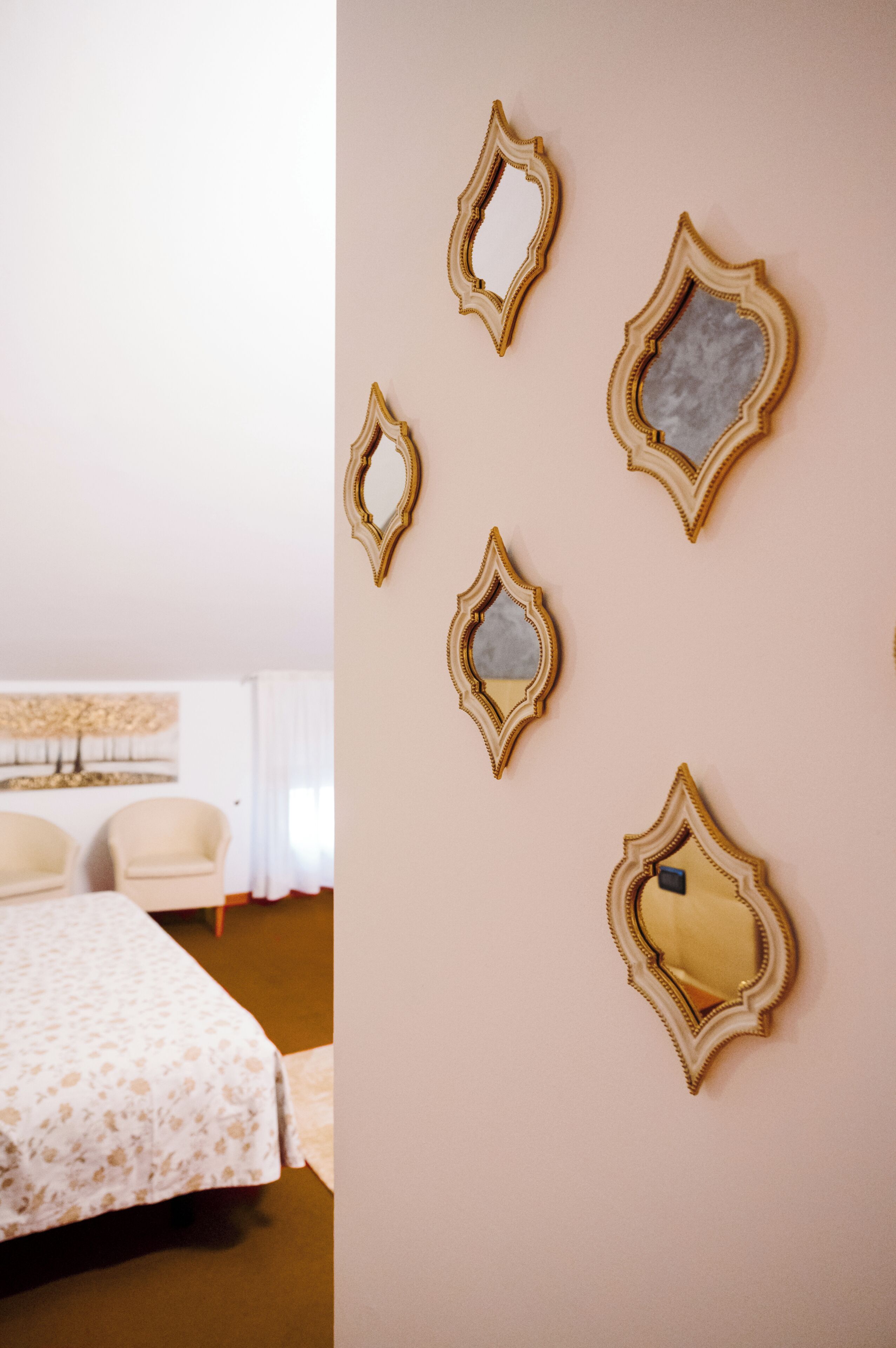 Una habitación de hotel con una cama, dos sillas y una pared con cinco espejos decorativos.
