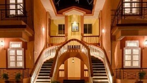 A hotel with a central archway leading to a balcony, surrounded by a pool reflecting the structure. - tio carmino resort (Calangute)
