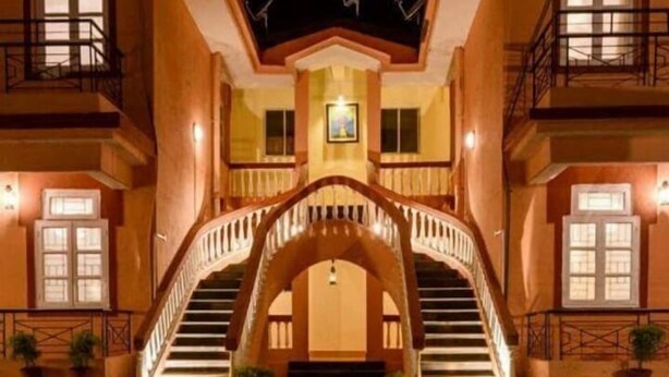 A hotel with a central archway leading to a balcony, surrounded by a pool reflecting the structure. - tio carmino resort (Calangute)