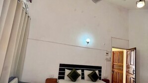 A bedroom with a bed, two chairs, a nightstand, a ceiling fan, and a door. - tio carmino resort (Calangute)