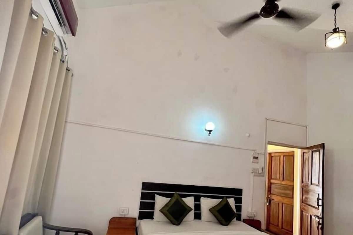 A bedroom with a bed, two chairs, a nightstand, a ceiling fan, and a door.