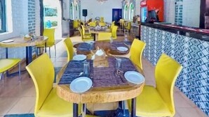 A restaurant with yellow chairs, a wooden table, and a ceiling with exposed beams. - tio carmino resort (Calangute)