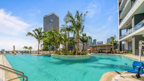 A swimming pool with a palm tree island, a lifeguard stand, and a view of a tall building in the background. - Bright Studio | Concierge | Near Miami Worldcenter (Miami)