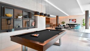 A modern pool table in a spacious, well-lit room with a contemporary design, including a seating area with a sofa and chairs, and a wall-mounted shelf with decorative items.