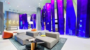 A modern lobby with a seating area featuring sofas and a coffee table, a reception desk, and a wall with vertical light fixtures.
