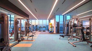 A modern gym with various exercise equipment, large windows, and a bright interior.