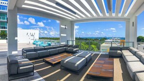 A rooftop terrace with a large sectional sofa, a wooden coffee table, and a view of the city skyline.