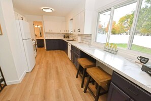 Une cuisine moderne avec un plan de travail en marbre, des tabourets en bois et une fenêtre donnant sur la verdure.