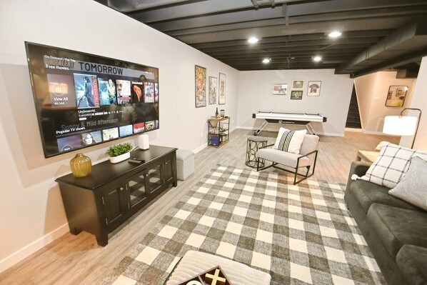A modern living room with a large flat-screen TV, a checkered rug, a sofa, a coffee table, and a pool table.