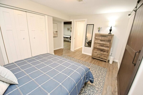A bedroom with a bed, a dresser, a mirror, and a door leading to another room.