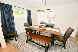 A dining area with a rectangular table, four chairs, a bench, a chandelier, and a rug.