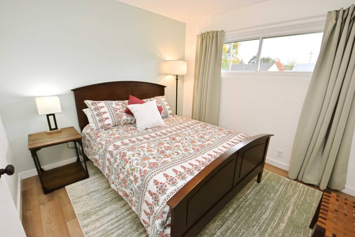 A bedroom with a bed, bedside tables, a lamp, a window with curtains, and a view of the outside.