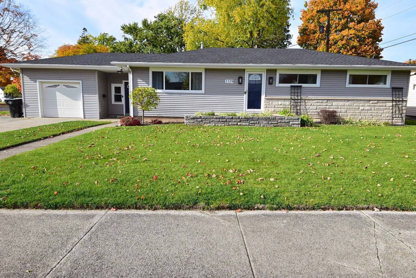 A single-story house with a garage, a small front yard, and a stone foundation.