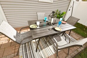 An outdoor patio with a table and chairs, a striped rug, and a potted plant.