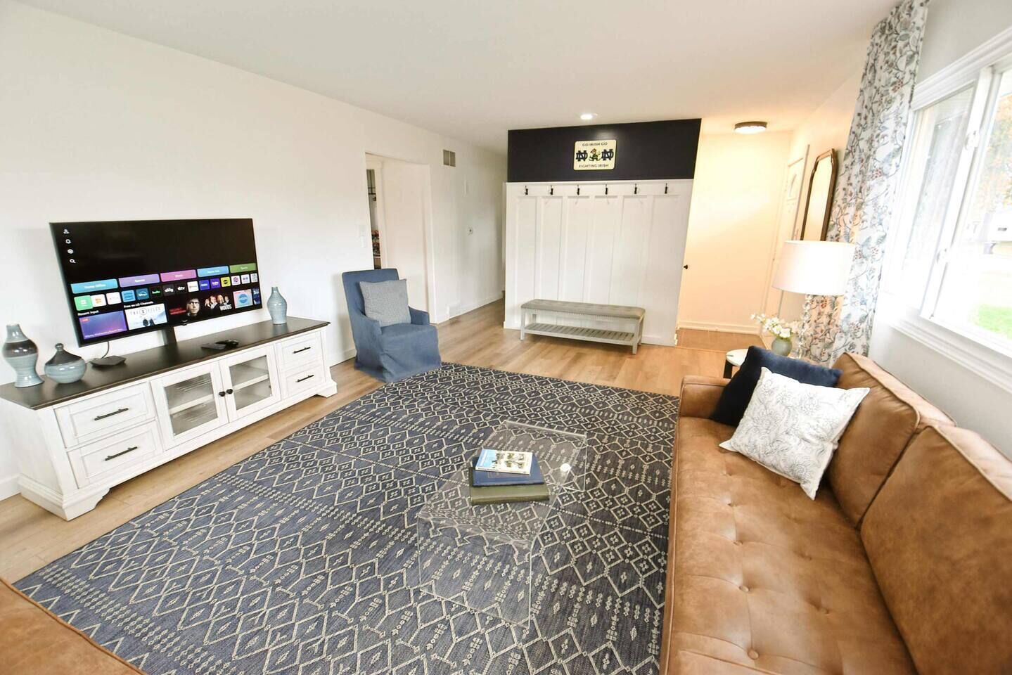 A living room with a flat-screen TV, a sofa, a patterned rug, and a bench.