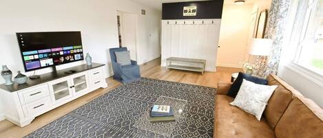 A living room with a flat-screen TV, a sofa, a patterned rug, and a bench.