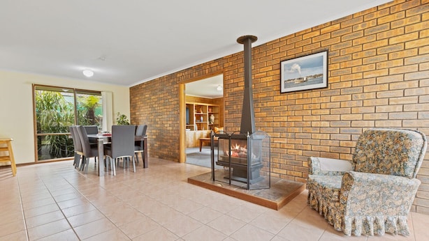 A spacious living area with a brick wall, a fireplace, a dining table with chairs, and a floral-patterned armchair. - The Hideaway: This holiday house is your gateway to unforgettable memories (Paynesville)