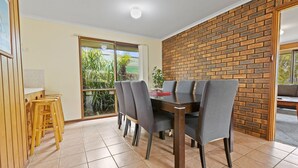 A dining area with a brick wall, a large window, and a view of greenery. - The Hideaway: This holiday house is your gateway to unforgettable memories (Paynesville)