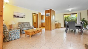 A living room with a sofa, a wooden coffee table, and a dining area with a table and chairs. - The Hideaway: This holiday house is your gateway to unforgettable memories (Paynesville)
