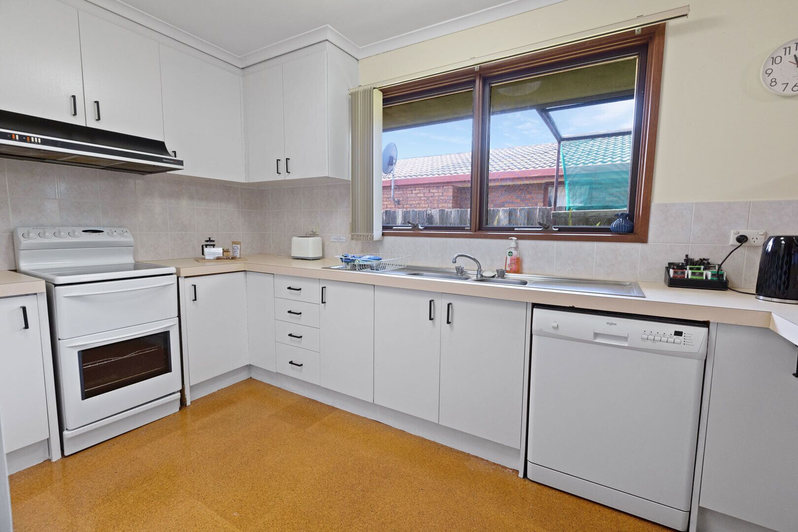A kitchen with white cabinets, a stove, a dishwasher, and a window with a view of a building.